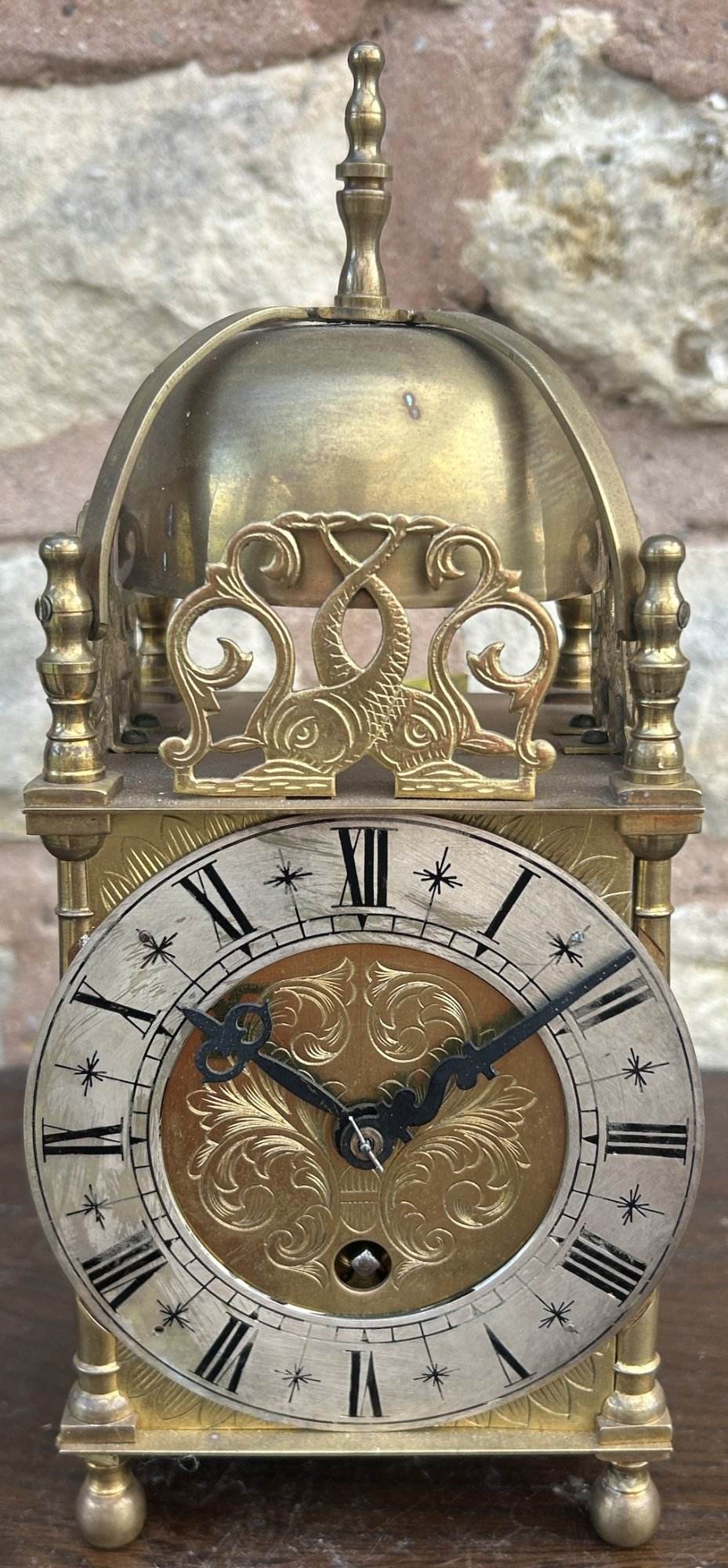 Lovely antique lantern mantel clock ca 1905. Wonderful original brass case with foliate decoration. Original silver chapter ring dial and hands. Fish finials to the front sides.